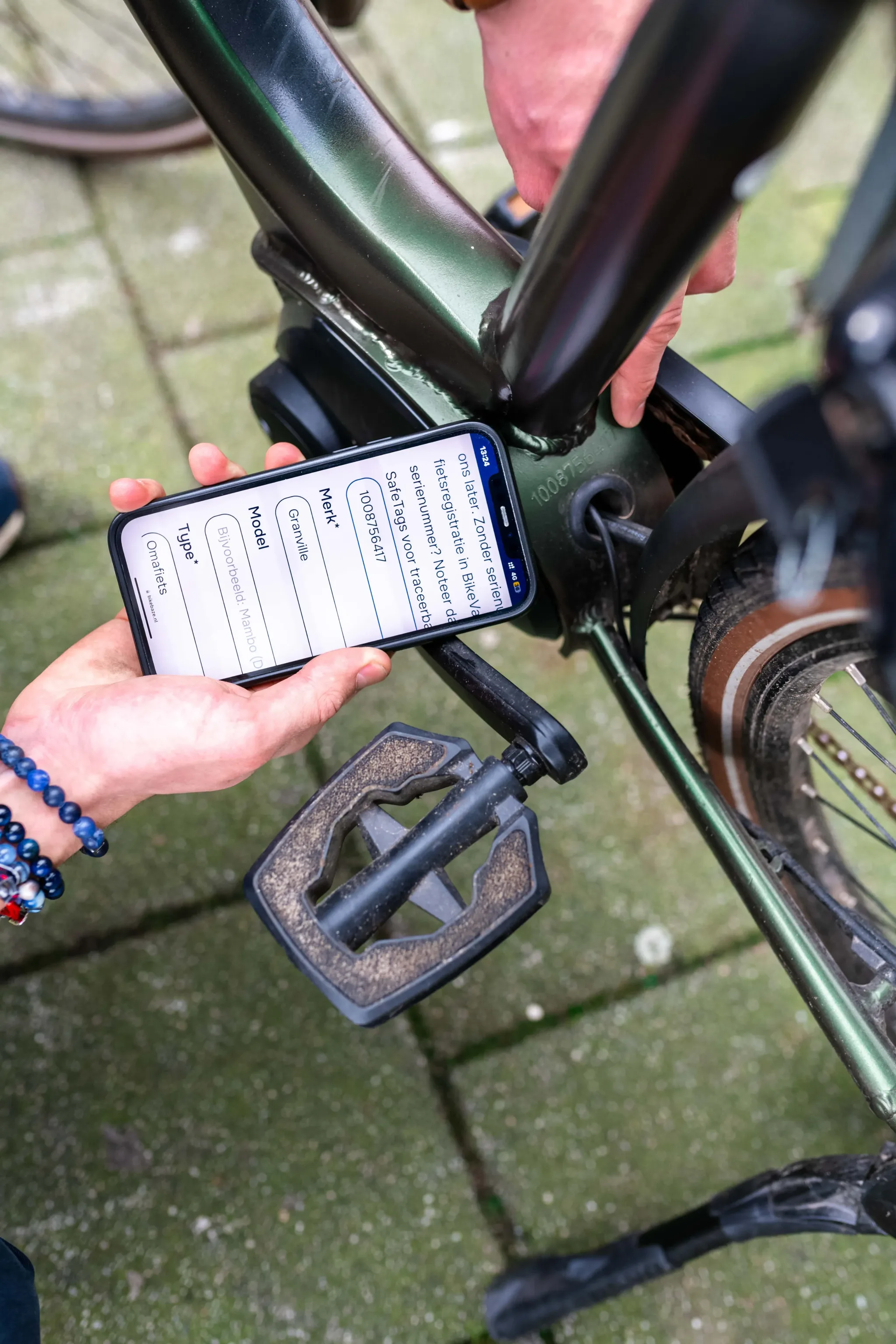 Someone checks a frame number on a green bike while another person enters details on a smartphone.